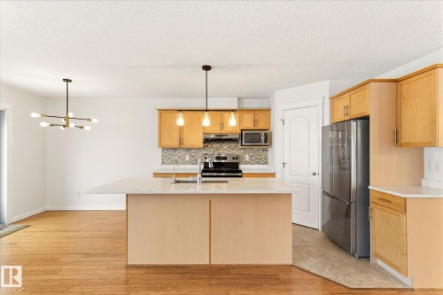 Kitchen island with a light-toned countertop, wood-finish cabinetry, stainless steel appliances, and mosaic tile backsplash - 2550 Rabbit Hill Road Nw, Edmonton, AB 