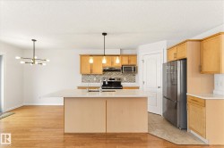 Kitchen island with a light-toned countertop, wood-finish cabinetry, stainless steel appliances, and mosaic tile backsplash - 