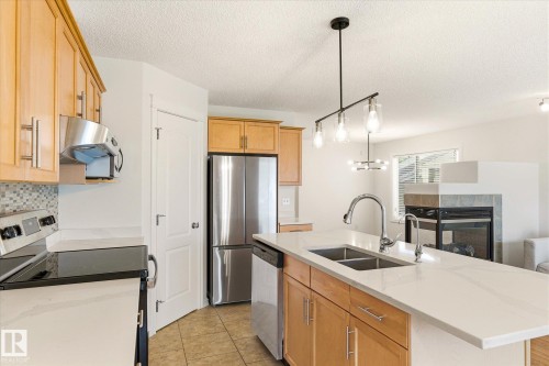 Kitchen featuring light wood cabinetry, white stone countertops, stainless steel appliances, and a mosaic tile backsplash - 2550 Rabbit Hill Road Nw, Edmonton, AB 