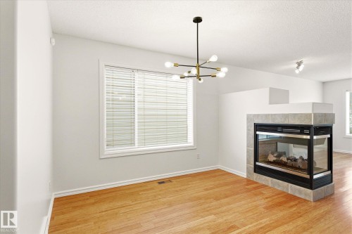 Hardwood flooring, tiled fireplace surround, contemporary chandelier, recessed lighting, and a large window with blinds - 2550 Rabbit Hill Road Nw, Edmonton, AB 