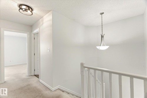 Hallway with neutral carpeting and white painted walls, featuring a semi-flush mount ceiling light and a contemporary pendant light - 2550 Rabbit Hill Road Nw, Edmonton, AB 