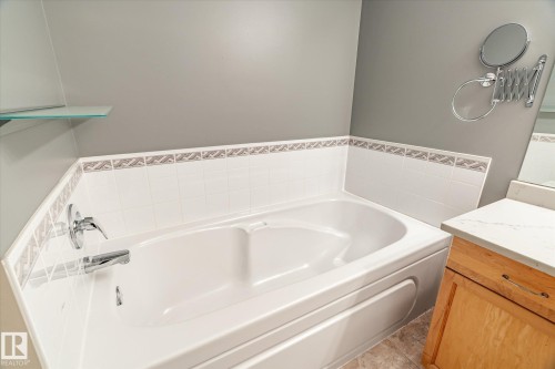 Built-in soaking tub with chrome fixtures, tile surround with decorative accent border, and a glass shelf - 2550 Rabbit Hill Road Nw, Edmonton, AB 