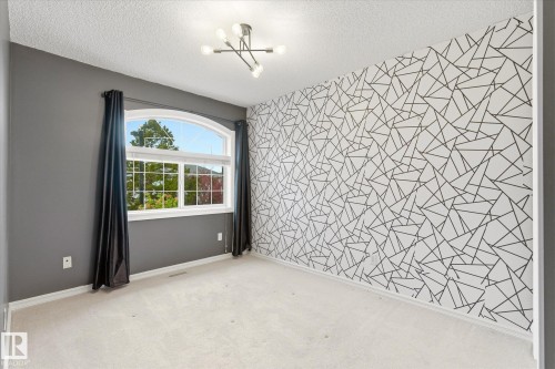 Arched window with gridded panes, modern ceiling light fixture, textured accent wall, and light-colored carpeting - 2550 Rabbit Hill Road Nw, Edmonton, AB 