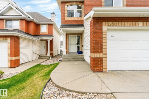 Brick and siding exterior with arched window detail, integrated garage, and concrete walkway - 2550 Rabbit Hill Road Nw, Edmonton, AB 
