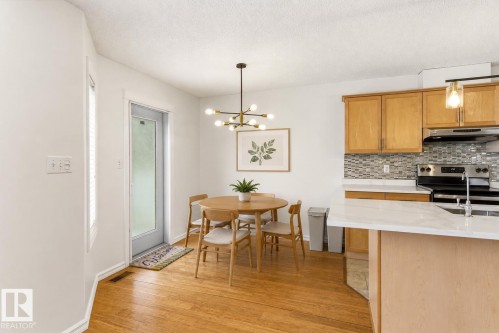 Wood-finish flooring throughout, with a contemporary chandelier, light wood cabinetry, and a tile backsplash in the kitchen area - 2550 Rabbit Hill Road Nw, Edmonton, AB 