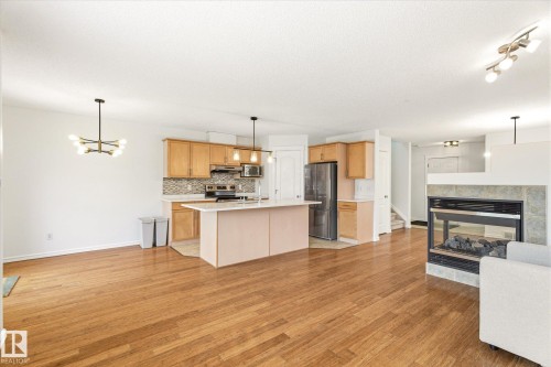 Open concept living area featuring wood-finish flooring, a kitchen island, light wood cabinetry, and a fireplace with a stone surround - 2550 Rabbit Hill Road Nw, Edmonton, AB 