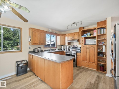 U-shaped kitchen featuring wood-finish cabinetry, stainless steel appliances, and wood-finish flooring - 7520 130 Avenue Nw, Edmonton, AB 