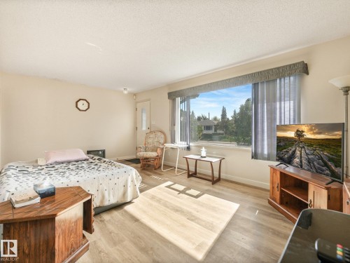 Wide window with vertical blinds, light-toned wood-finish flooring, and a white entry door - 7520 130 Avenue Nw, Edmonton, AB 