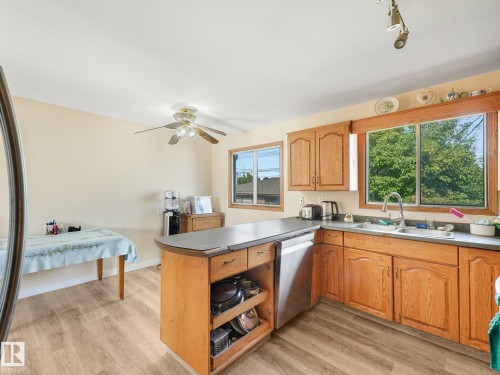 Kitchen featuring wood-finish flooring, wood cabinetry, a stainless steel dishwasher, and a double basin sink - 7520 130 Avenue Nw, Edmonton, AB 