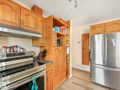 Wood-finish cabinetry with display shelving, stainless steel appliance suite, range hood, and wood-finish flooring - 7520 130 Avenue Nw, Edmonton, AB 