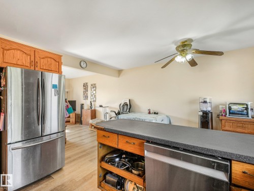 Kitchen featuring wood cabinetry, stainless steel refrigerator, dark countertop, and integrated dishwasher - 7520 130 Avenue Nw, Edmonton, AB 