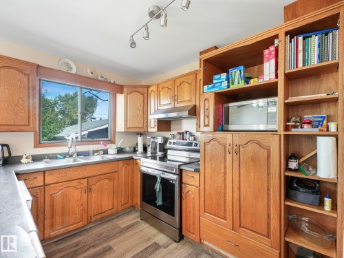 Wood-finish cabinetry, stainless steel range, track lighting, dual basin sink, and wood-finish flooring - 7520 130 Avenue Nw, Edmonton, AB 