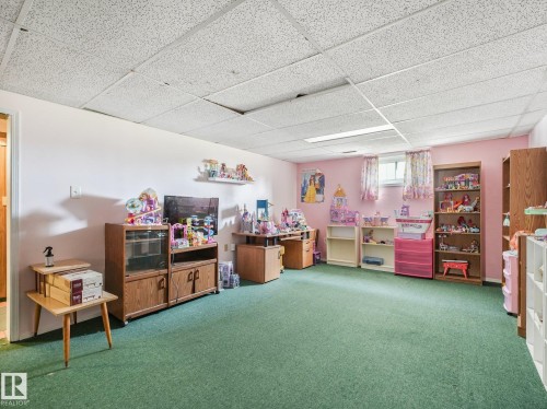 Recessed ceiling with acoustic tiles, window with white trim, wall-mounted shelf, light-colored walls, and green carpet flooring - 7520 130 Avenue Nw, Edmonton, AB 