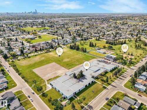Expansive urban landscape with a visible cityscape in the distance, featuring a large green field, multiple residential properties, and a prominent institutional building - 7520 130 Avenue Nw, Edmonton, AB 