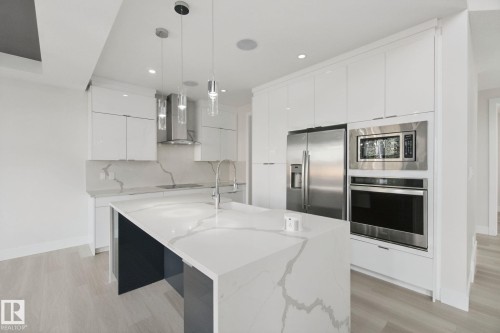 Modern kitchen featuring a waterfall island, integrated stainless steel appliances, white gloss cabinetry, and pendant lighting - 3699 Hummingbird Way Nw, Edmonton, AB 