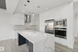 Modern kitchen featuring a waterfall island, integrated stainless steel appliances, white gloss cabinetry, and pendant lighting - 