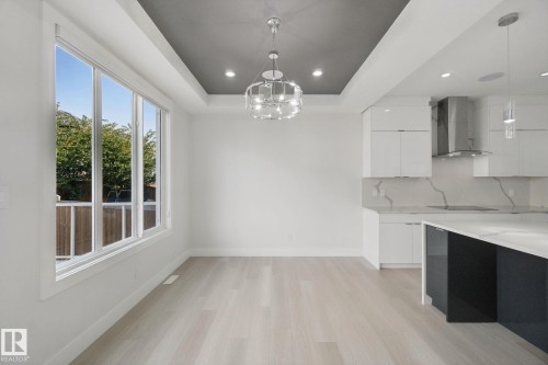 Recessed ceiling with an accent color, contemporary chandelier, large picture window, light wood-finish flooring, and white cabinetry - 3699 Hummingbird Way Nw, Edmonton, AB 