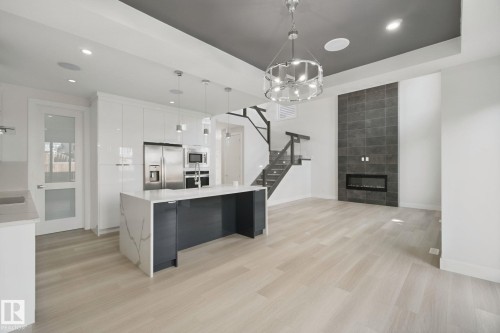 Open-concept living space with light wood-finish flooring, a contemporary kitchen island featuring a waterfall countertop, and stainless steel appliances - 3699 Hummingbird Way Nw, Edmonton, AB 
