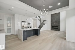 Open-concept living space with light wood-finish flooring, a contemporary kitchen island featuring a waterfall countertop, and stainless steel appliances - 