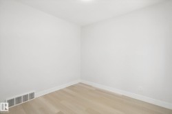 Light wood-finish flooring with white baseboards, bright white walls, and an overhead flush-mount light fixture - 