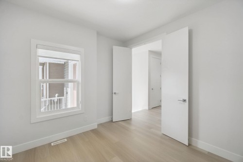 Light wood-finish flooring with white baseboards, a white-framed window, and white interior doors with contemporary hardware - 3699 Hummingbird Way Nw, Edmonton, AB 