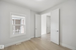 Light wood-finish flooring with white baseboards, a white-framed window, and white interior doors with contemporary hardware - 