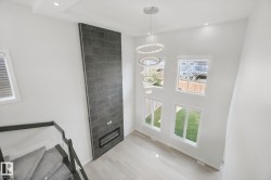 Two-story living area featuring a full-height tile fireplace surround, linear electric fireplace, and a multi-tiered chandelier - 