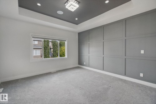 Recessed ceiling with integrated lighting, modern chandelier, accent wall with panel molding, large window with roller shade, and light-tone carpeting - 3699 Hummingbird Way Nw, Edmonton, AB 
