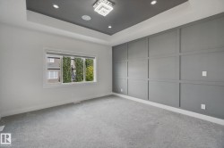 Recessed ceiling with integrated lighting, modern chandelier, accent wall with panel molding, large window with roller shade, and light-tone carpeting - 