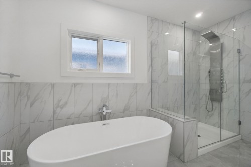 Freestanding oval soaking tub, glass-enclosed shower, wall-mounted shower panel, and light-toned tile flooring - 3699 Hummingbird Way Nw, Edmonton, AB 