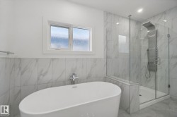 Freestanding oval soaking tub, glass-enclosed shower, wall-mounted shower panel, and light-toned tile flooring - 