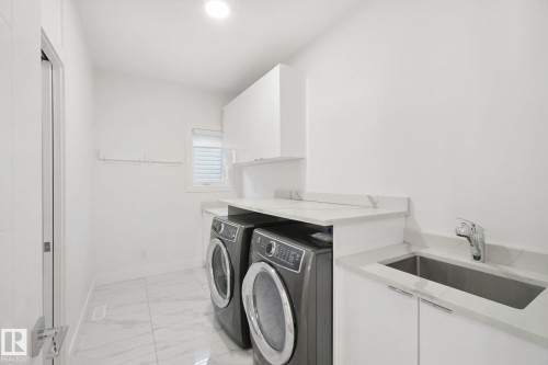 Dedicated laundry area featuring a stainless steel sink, chrome faucet, white cabinetry, and a window for natural light - 3699 Hummingbird Way Nw, Edmonton, AB 
