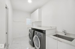 Dedicated laundry area featuring a stainless steel sink, chrome faucet, white cabinetry, and a window for natural light - 