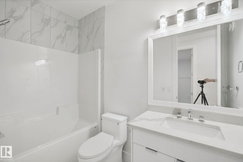 White bathroom featuring a built-in tub with a shower, toilet, vanity with integrated sink, and an illuminated mirror - 3699 Hummingbird Way Nw, Edmonton, AB 
