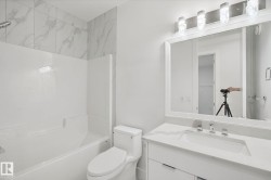 White bathroom featuring a built-in tub with a shower, toilet, vanity with integrated sink, and an illuminated mirror - 
