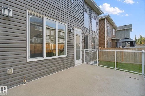 Concrete patio with glass railing, featuring gray siding and white-framed windows - 3699 Hummingbird Way Nw, Edmonton, AB 