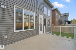 Concrete patio with glass railing, featuring gray siding and white-framed windows - 