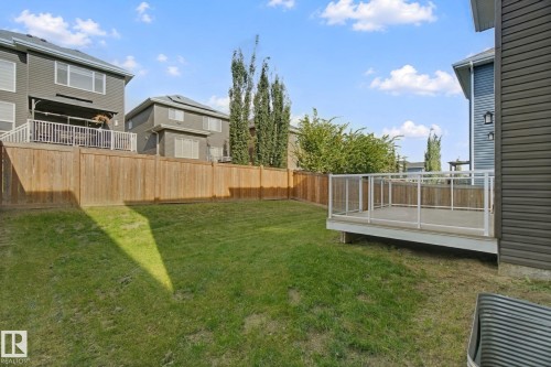 Expansive rear yard featuring a manicured lawn, full privacy fencing, and a raised composite deck with glass panel railing - 3699 Hummingbird Way Nw, Edmonton, AB 