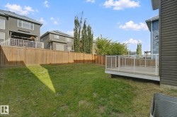 Expansive rear yard featuring a manicured lawn, full privacy fencing, and a raised composite deck with glass panel railing - 