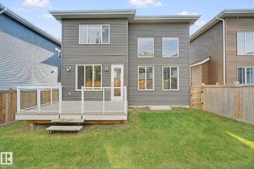 Gray horizontal siding, multi-pane windows, elevated wood deck with glass railing, sliding glass door, and a grass lawn - 3699 Hummingbird Way Nw, Edmonton, AB 