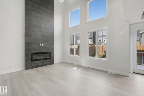 Two-story tiled fireplace with an integrated electric insert, light wood-finish flooring, and multiple large windows - 3699 Hummingbird Way Nw, Edmonton, AB 
