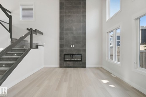 Two-story living area featuring a tile-surround fireplace, large windows, wood-finish flooring, and a staircase with glass railings - 3699 Hummingbird Way Nw, Edmonton, AB 