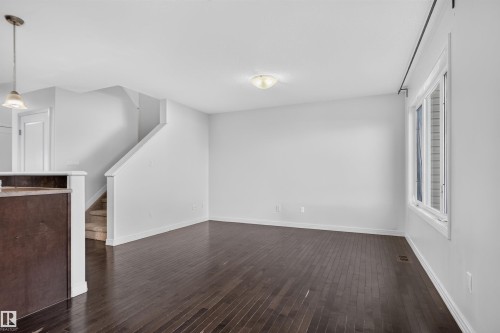 Spacious living area featuring wood-finish flooring, a large window, white walls, and a staircase with carpeted treads - 2145 28 Street Nw, Edmonton, AB 