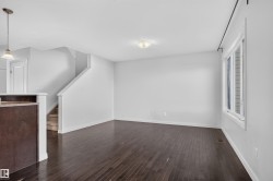 Spacious living area featuring wood-finish flooring, a large window, white walls, and a staircase with carpeted treads - 
