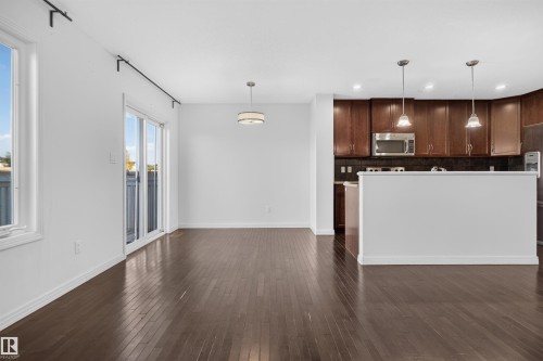 Hardwood flooring throughout, kitchen with dark wood cabinetry, stainless steel microwave, black tile backsplash, and two pendant lights - 2145 28 Street Nw, Edmonton, AB 