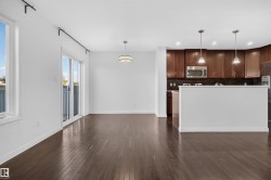 Hardwood flooring throughout, kitchen with dark wood cabinetry, stainless steel microwave, black tile backsplash, and two pendant lights - 