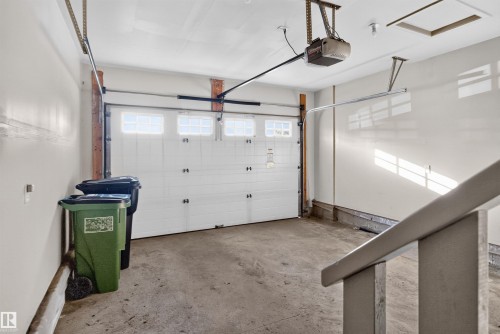 Attached garage featuring a white overhead door with upper window panels, exposed wood framing, and a concrete floor - 2145 28 Street Nw, Edmonton, AB 