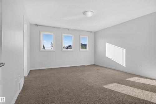Neutral wall tones, carpeted flooring, three windows with white trim, and a ceiling-mounted light fixture - 2145 28 Street Nw, Edmonton, AB 
