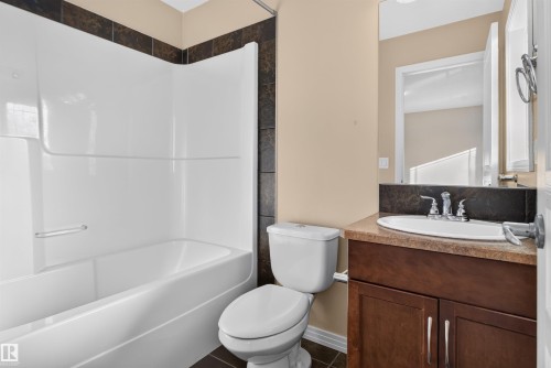 White tub and shower combination with dark tile surround, dark wood-finish vanity with countertop, and undermount sink with chrome fixtures - 2145 28 Street Nw, Edmonton, AB 
