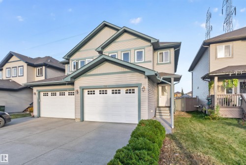 Two-story residence featuring light-toned siding, a double attached garage with white doors, and a concrete driveway - 2145 28 Street Nw, Edmonton, AB 